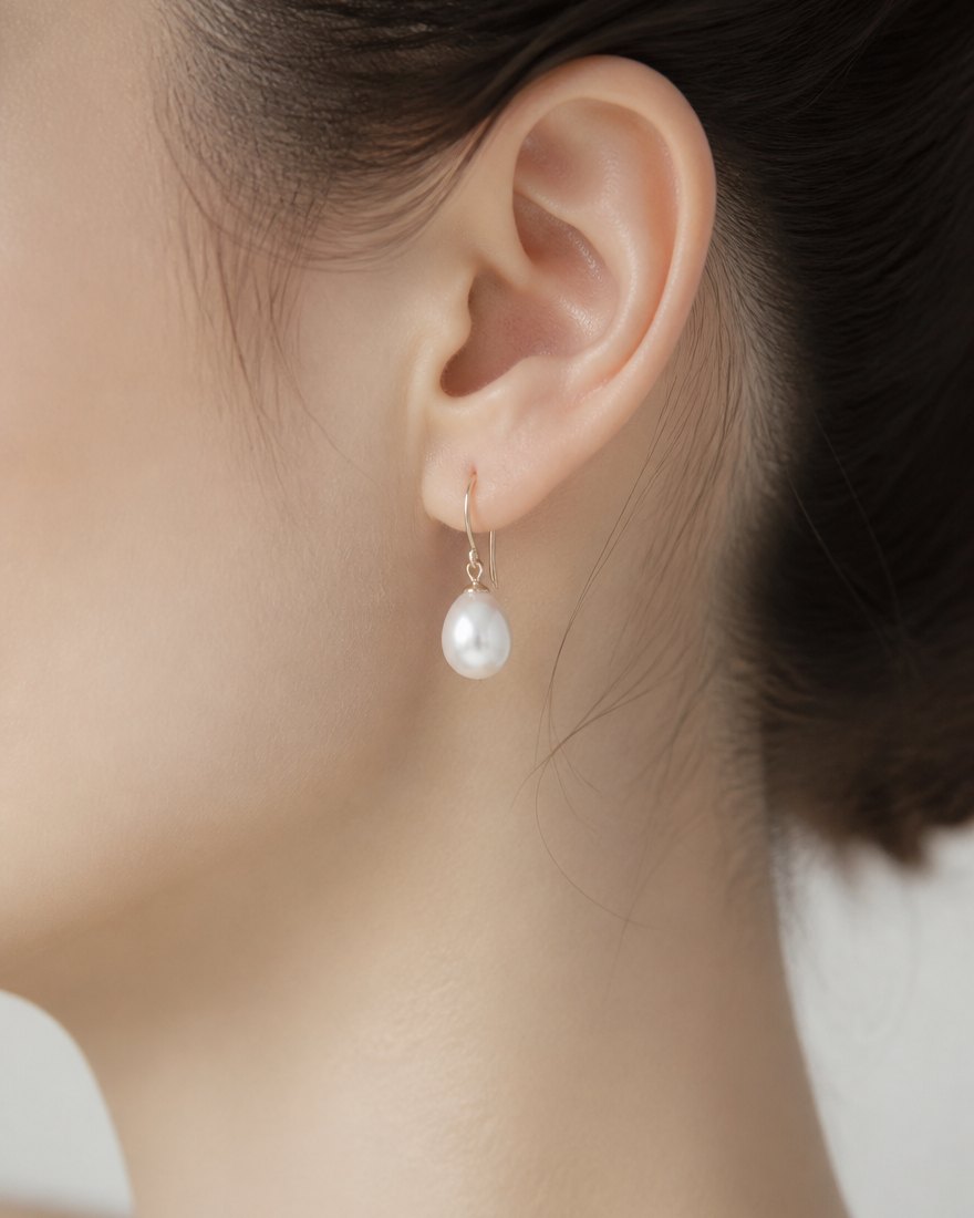 Pearl drop earring worn, soft studio light